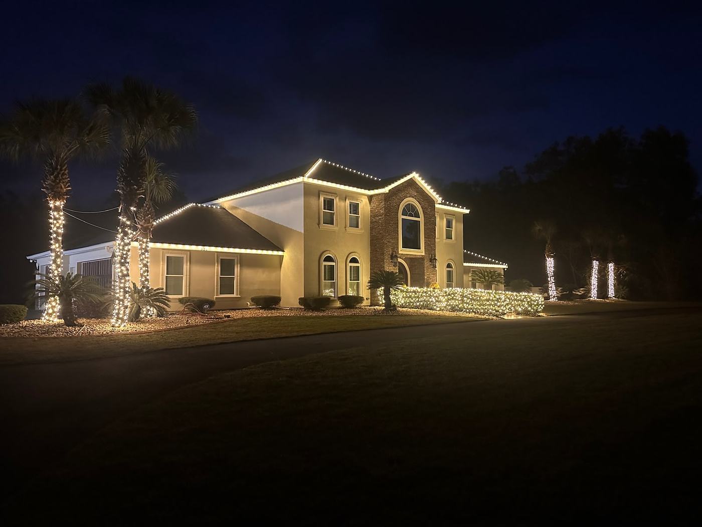 Warm white roofline lighting and wrapped palms on a Windermere stucco home